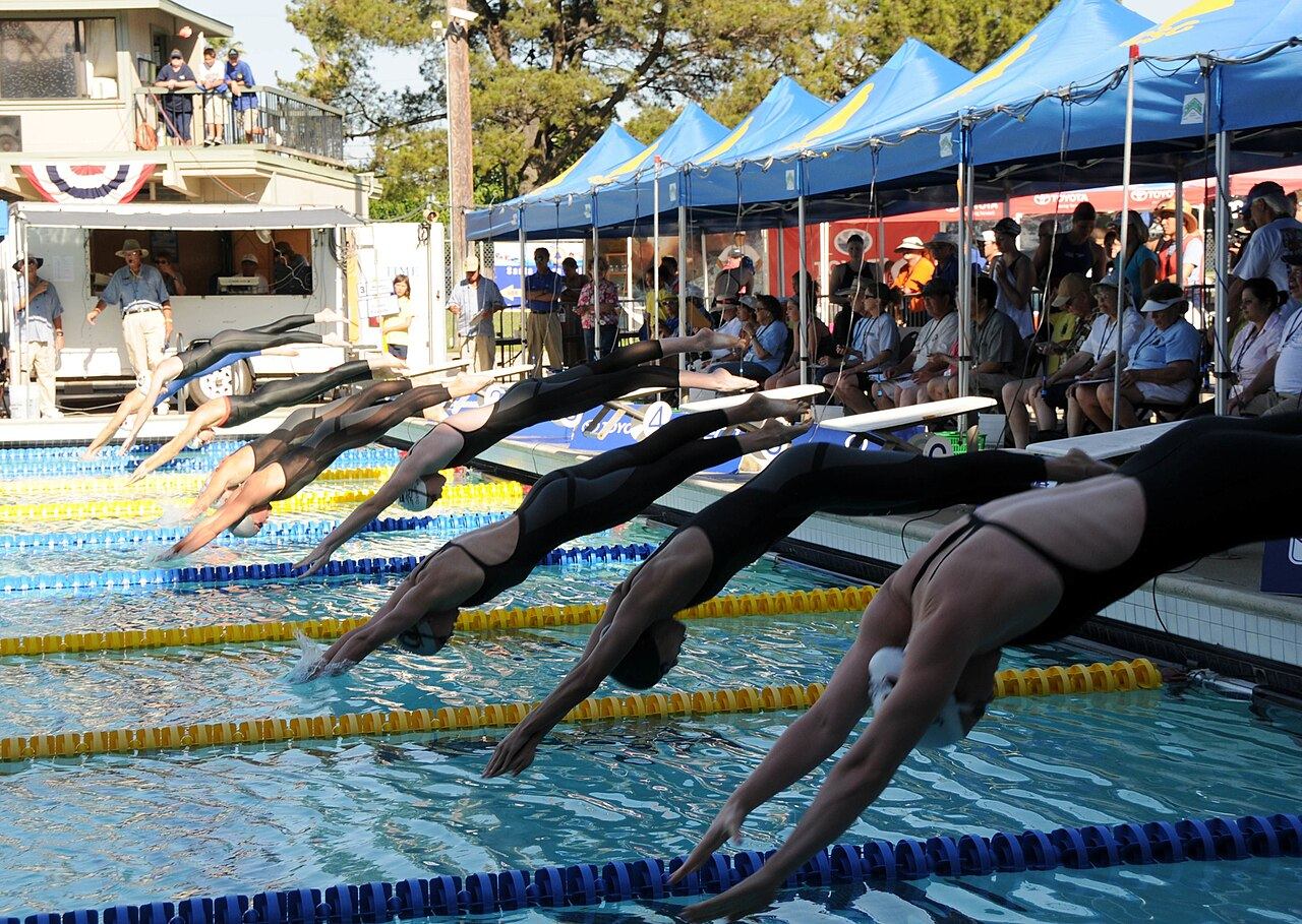 Swimmers diving off the blocks at the start of a race at an outdoor club swim meet